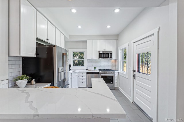 kitchen with a peninsula, light stone countertops, stainless steel appliances, white cabinetry, and a wealth of natural light