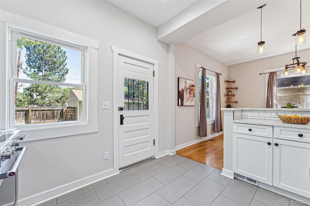 kitchen with light tile patterned floors, hanging light fixtures, plenty of natural light, and white cabinets