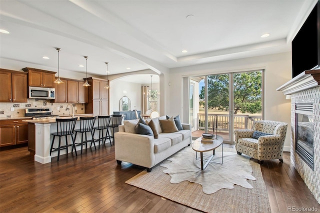 living area featuring a glass covered fireplace, recessed lighting, dark wood-style floors, and arched walkways