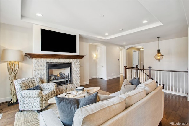 living area with a tray ceiling, arched walkways, and wood finished floors