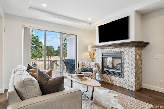 living room featuring a multi sided fireplace, a tray ceiling, baseboards, and wood finished floors