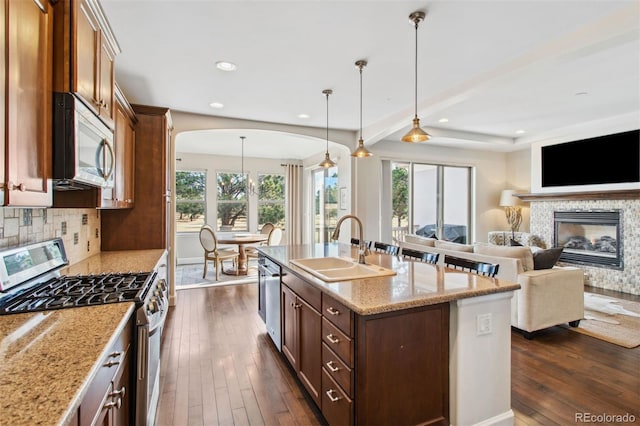 kitchen with a sink, stainless steel appliances, decorative backsplash, a multi sided fireplace, and dark wood-style flooring