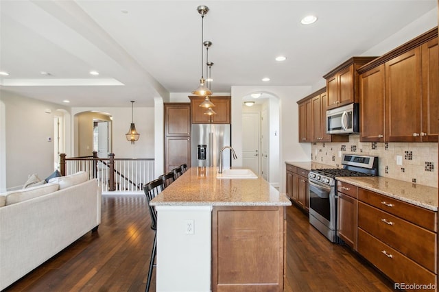 kitchen featuring open floor plan, appliances with stainless steel finishes, a kitchen breakfast bar, arched walkways, and a sink