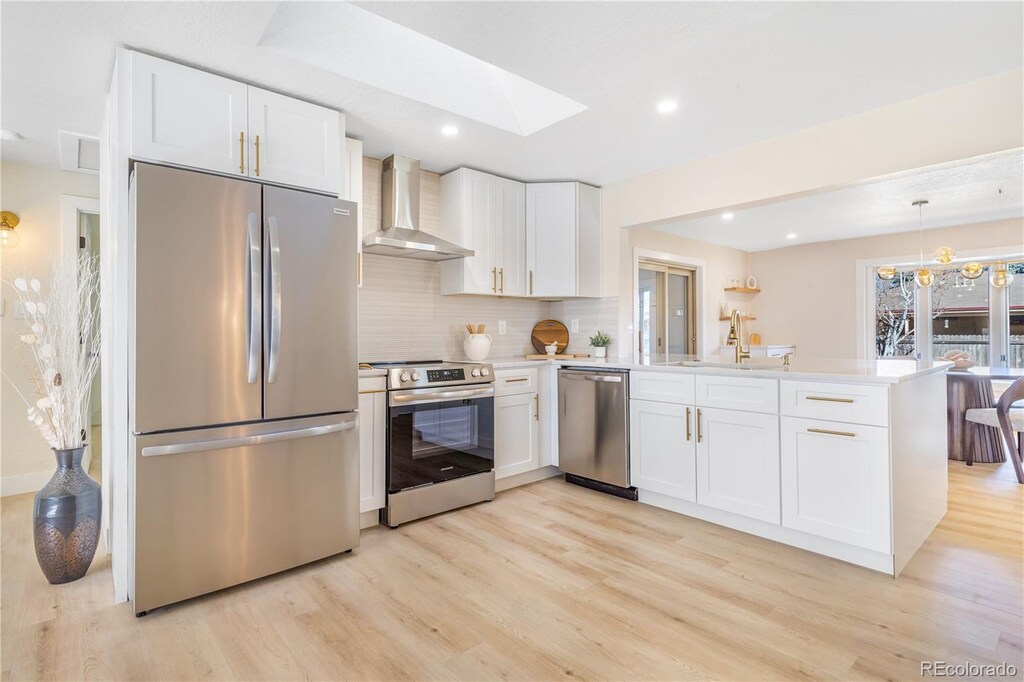 1240 S Chase Ct, Lakewood, CO 80232 - kitchen with a peninsula, appliances with stainless steel finishes, wall chimney range hood, and light wood-style floors