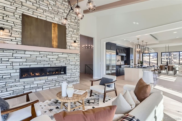 living room featuring beamed ceiling, a fireplace, light hardwood / wood-style floors, and a notable chandelier