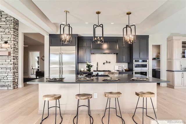 kitchen featuring custom exhaust hood, appliances with stainless steel finishes, a breakfast bar area, and a spacious island