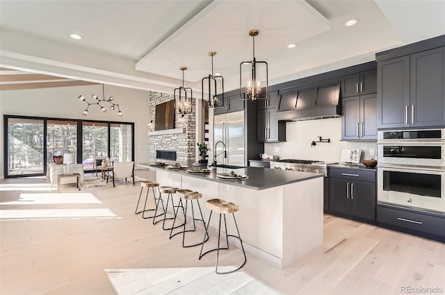 kitchen featuring appliances with stainless steel finishes, pendant lighting, a kitchen bar, wall chimney range hood, and a center island with sink