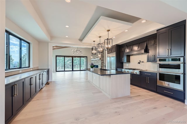 5820 Powell Rd, Parker, CO 80134 - kitchen with a tray ceiling, custom range hood, a chandelier, appliances with stainless steel finishes, and light wood finished floors