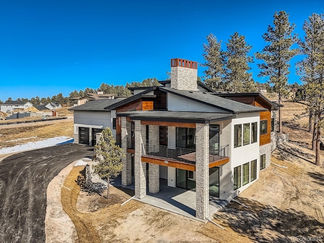 5820 Powell Rd, Parker, CO 80134 - back of property featuring a chimney, stone siding, a patio area, roof with shingles, and a garage