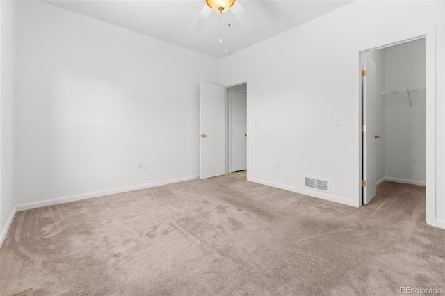 unfurnished bedroom featuring ceiling fan, a spacious closet, light carpet, and a closet