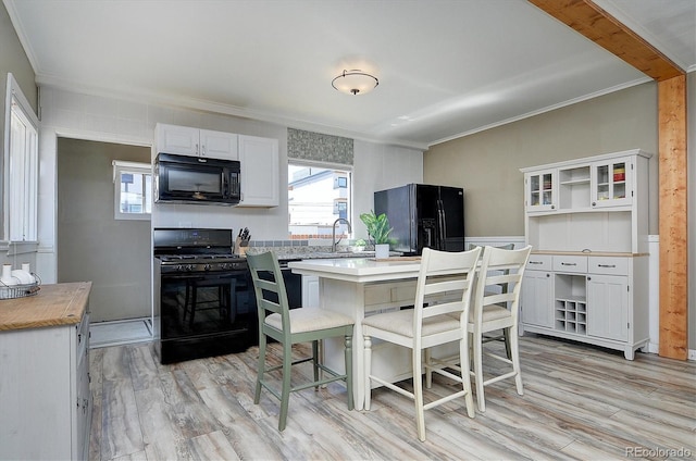 kitchen featuring white cabinets, light wood-style flooring, black appliances, and ornamental molding