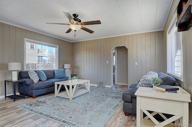 living area featuring crown molding, arched walkways, a ceiling fan, light wood finished floors, and baseboards