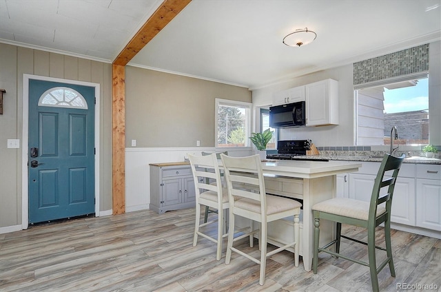 kitchen featuring white cabinets, a sink, ornamental molding, black appliances, and light wood-style flooring