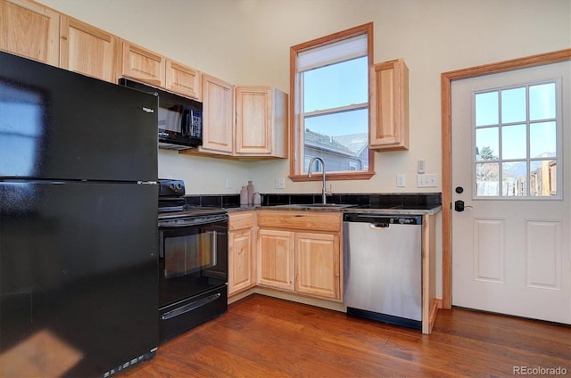 kitchen featuring a sink, black appliances, light brown cabinetry, and dark countertops