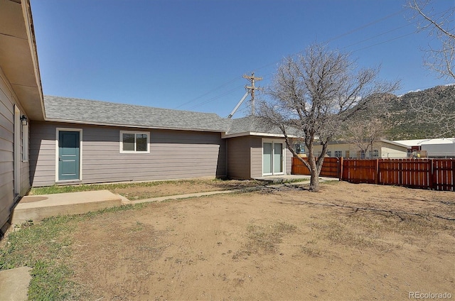 rear view of property featuring a shingled roof and fence