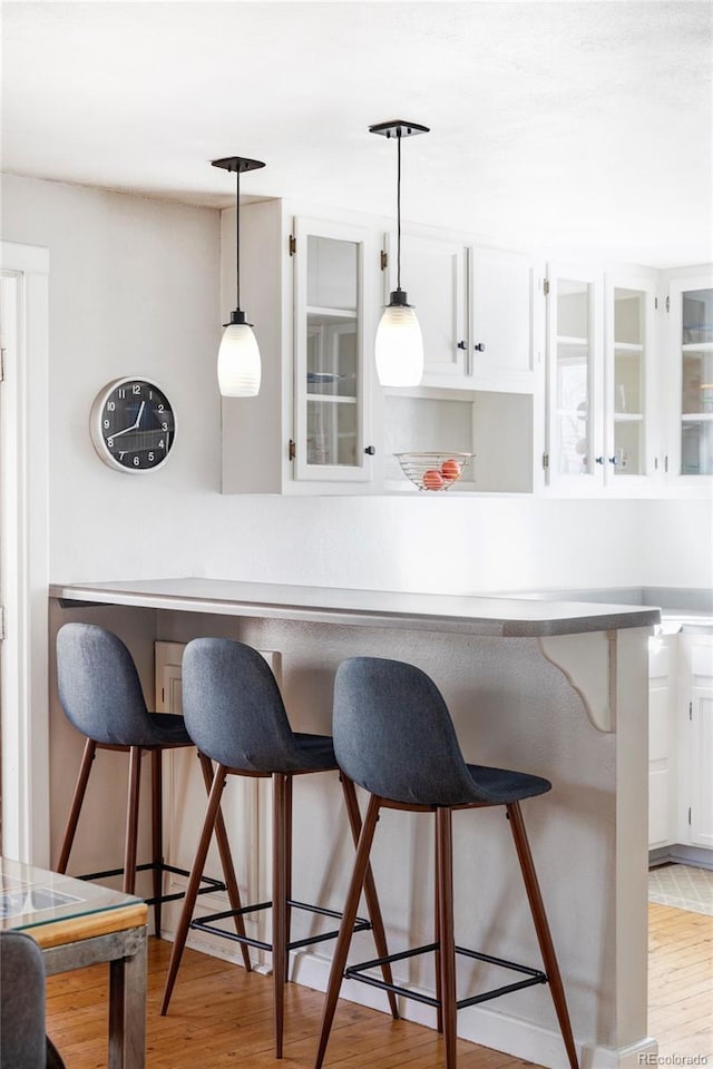 kitchen featuring decorative light fixtures, white cabinets, a kitchen breakfast bar, and light hardwood / wood-style floors