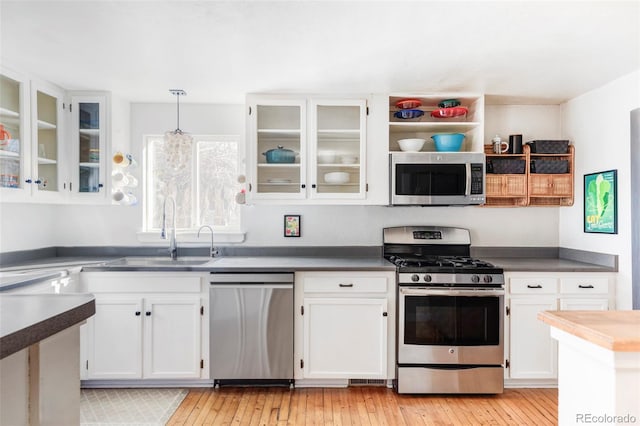 kitchen featuring appliances with stainless steel finishes, hanging light fixtures, light hardwood / wood-style floors, sink, and white cabinetry