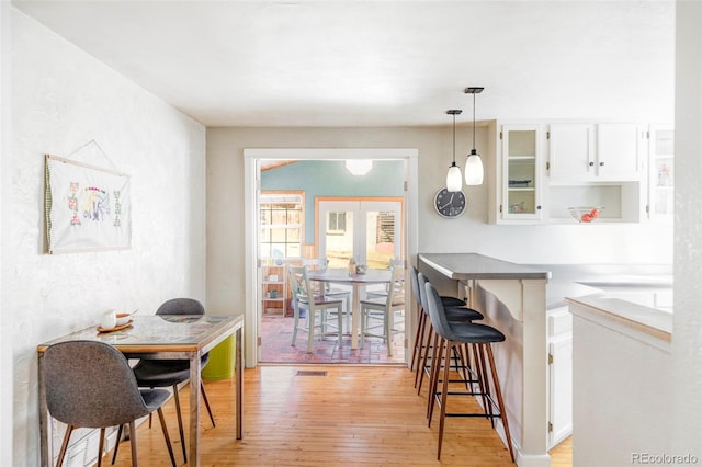 kitchen with kitchen peninsula, pendant lighting, light wood-type flooring, a breakfast bar area, and white cabinetry