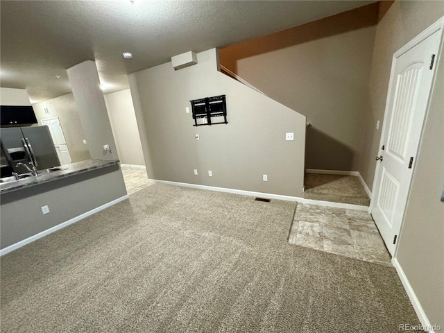 unfurnished living room featuring light carpet, sink, and a textured ceiling