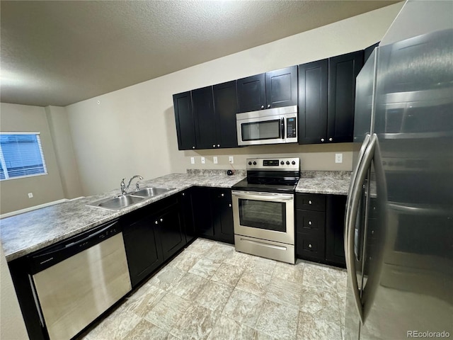 kitchen featuring sink, stainless steel appliances, light stone counters, kitchen peninsula, and a textured ceiling