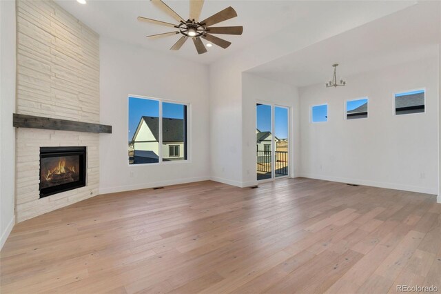 unfurnished living room featuring a stone fireplace, ceiling fan with notable chandelier, and light hardwood / wood-style flooring