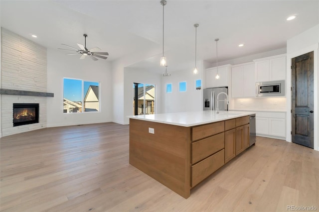 kitchen with a stone fireplace, sink, white cabinets, a large island with sink, and stainless steel appliances