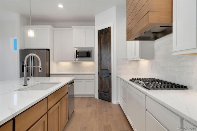 kitchen with appliances with stainless steel finishes, white cabinetry, light stone countertops, custom range hood, and decorative light fixtures