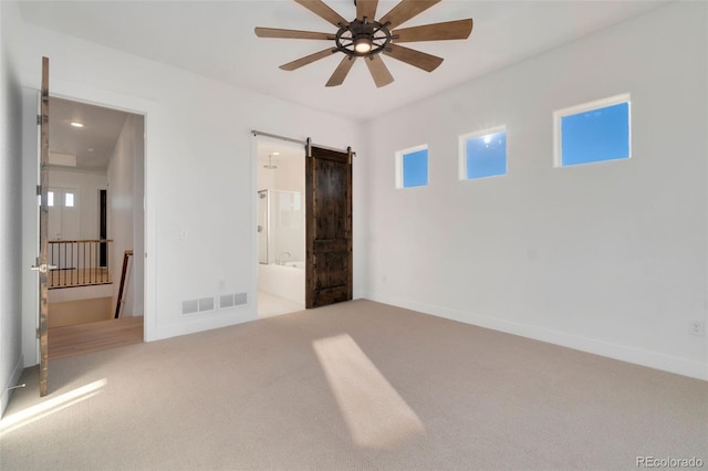 unfurnished bedroom featuring ceiling fan, ensuite bath, a barn door, and carpet flooring