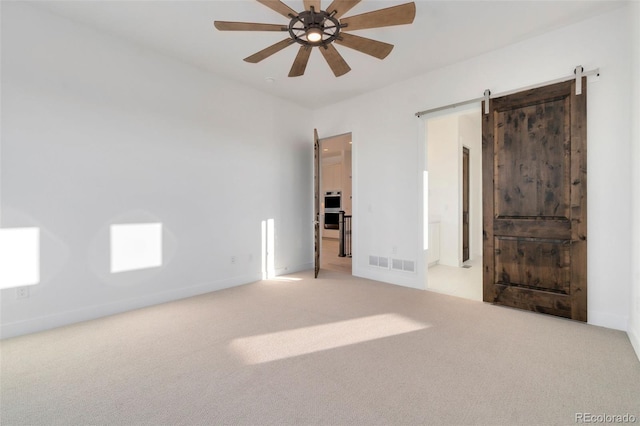 carpeted empty room with ceiling fan and a barn door