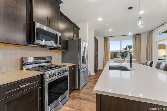 kitchen with appliances with stainless steel finishes, decorative backsplash, light wood-type flooring, pendant lighting, and sink