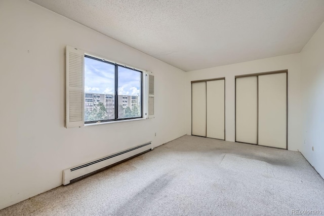 unfurnished bedroom with carpet flooring, baseboard heating, two closets, and a textured ceiling