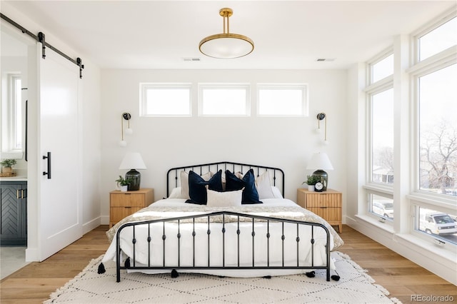 bedroom featuring multiple windows, light hardwood / wood-style flooring, and a barn door