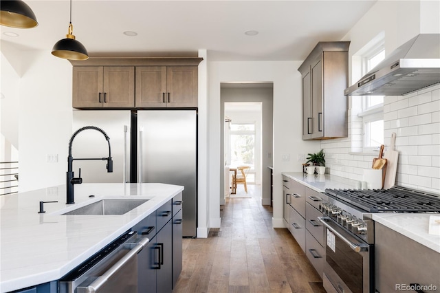 kitchen with appliances with stainless steel finishes, sink, light stone counters, wall chimney exhaust hood, and hanging light fixtures