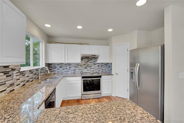 11091 Clayton St, Northglenn, CO 80233 - kitchen featuring appliances with stainless steel finishes, under cabinet range hood, light stone countertops, light wood-style floors, and tasteful backsplash