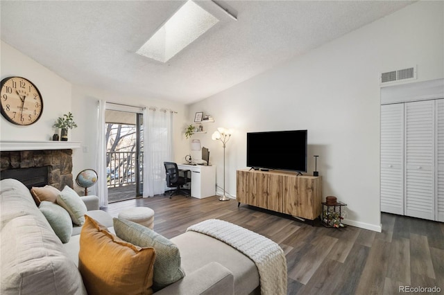 living area featuring visible vents, wood finished floors, a stone fireplace, a textured ceiling, and vaulted ceiling with skylight