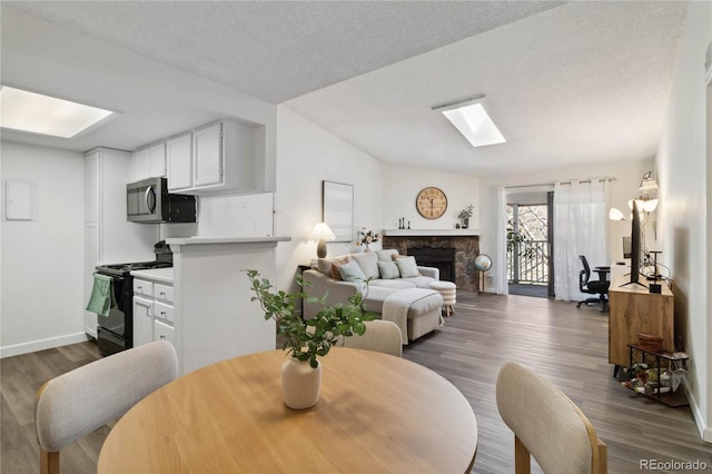 living area with a stone fireplace, dark wood-style flooring, baseboards, and a skylight