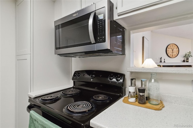 kitchen featuring white cabinets, stainless steel microwave, and black range with electric stovetop