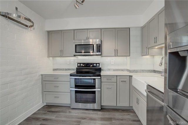 kitchen with appliances with stainless steel finishes, tasteful backsplash, gray cabinetry, brick wall, and light hardwood / wood-style floors