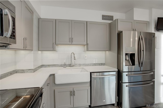 kitchen featuring backsplash, stainless steel appliances, gray cabinets, and sink