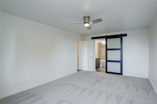 unfurnished bedroom featuring carpet flooring, ceiling fan, a barn door, and connected bathroom