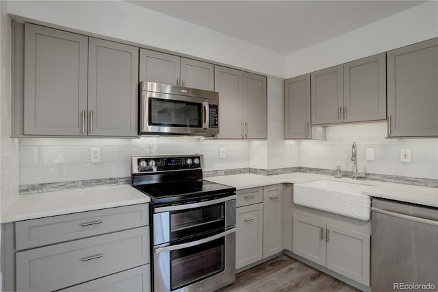 kitchen with light wood finished floors, gray cabinets, decorative backsplash, appliances with stainless steel finishes, and a sink