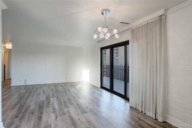 empty room featuring light wood-style floors, ornamental molding, brick wall, a chandelier, and baseboards