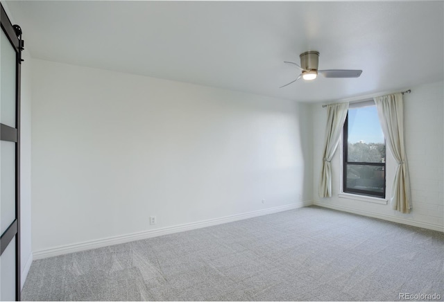 unfurnished room with light carpet, ceiling fan, a barn door, and baseboards