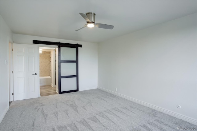 unfurnished bedroom with a barn door, a ceiling fan, light carpet, connected bathroom, and baseboards