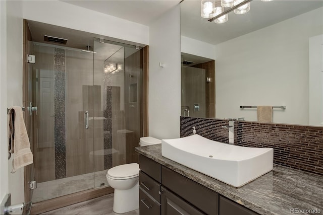 bathroom with a stall shower, decorative backsplash, toilet, wood finished floors, and vanity