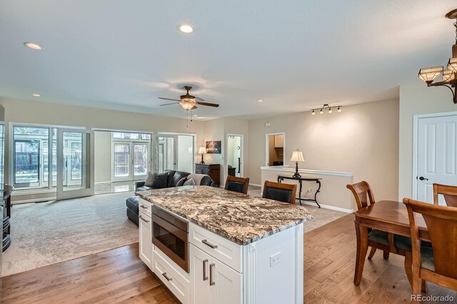 5461 S Youngfield Ct, Littleton, CO 80127 - kitchen featuring stainless steel microwave, open floor plan, white cabinetry, a ceiling fan, and light stone countertops