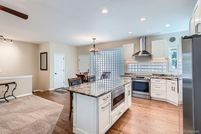 5461 S Youngfield Ct, Littleton, CO 80127 - kitchen with stainless steel appliances, wall chimney range hood, a breakfast bar area, white cabinetry, and dark stone counters