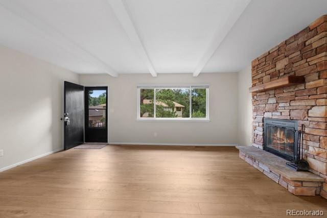 unfurnished living room with beam ceiling, a stone fireplace, and light hardwood / wood-style flooring