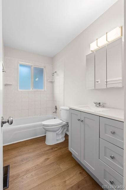 full bathroom featuring vanity, wood-type flooring, tiled shower / bath combo, and toilet