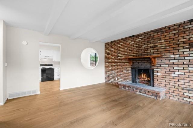 unfurnished living room with beam ceiling, light hardwood / wood-style flooring, and a brick fireplace